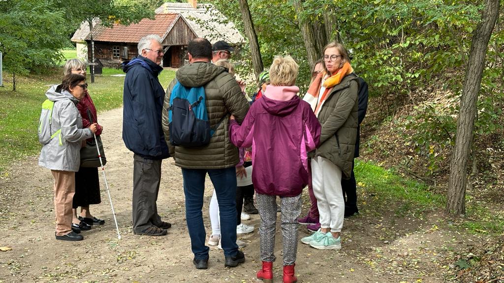 Opiekunowie, beneficjenci i przewodnik podczas zwiedzania Muzeum Wsi Mazowieckiej